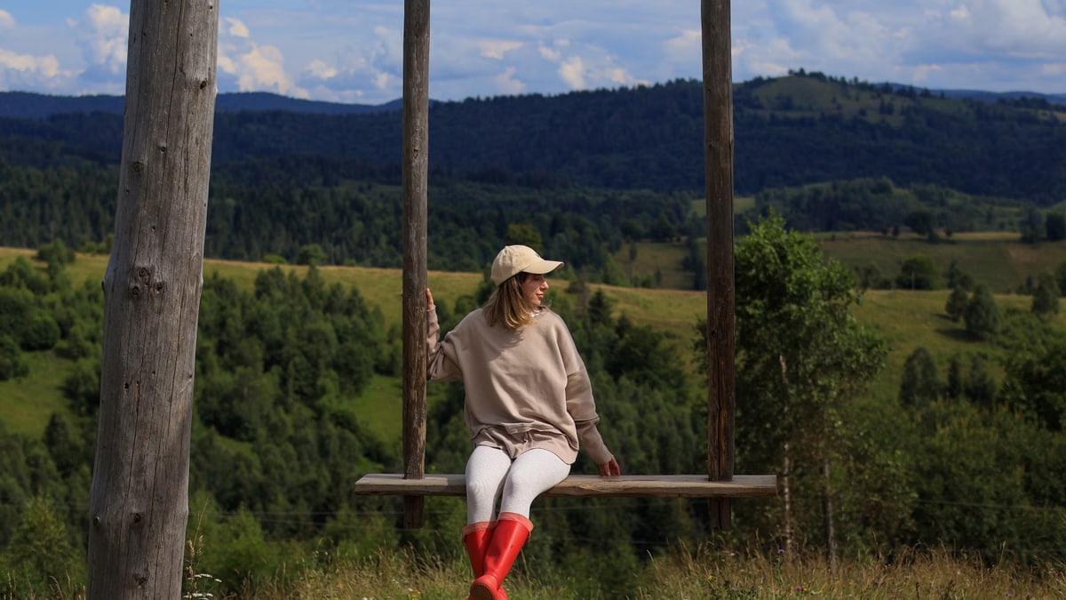 A woman in casual attire enjoys a swing with a scenic mountain view, embracing leisure and nature.